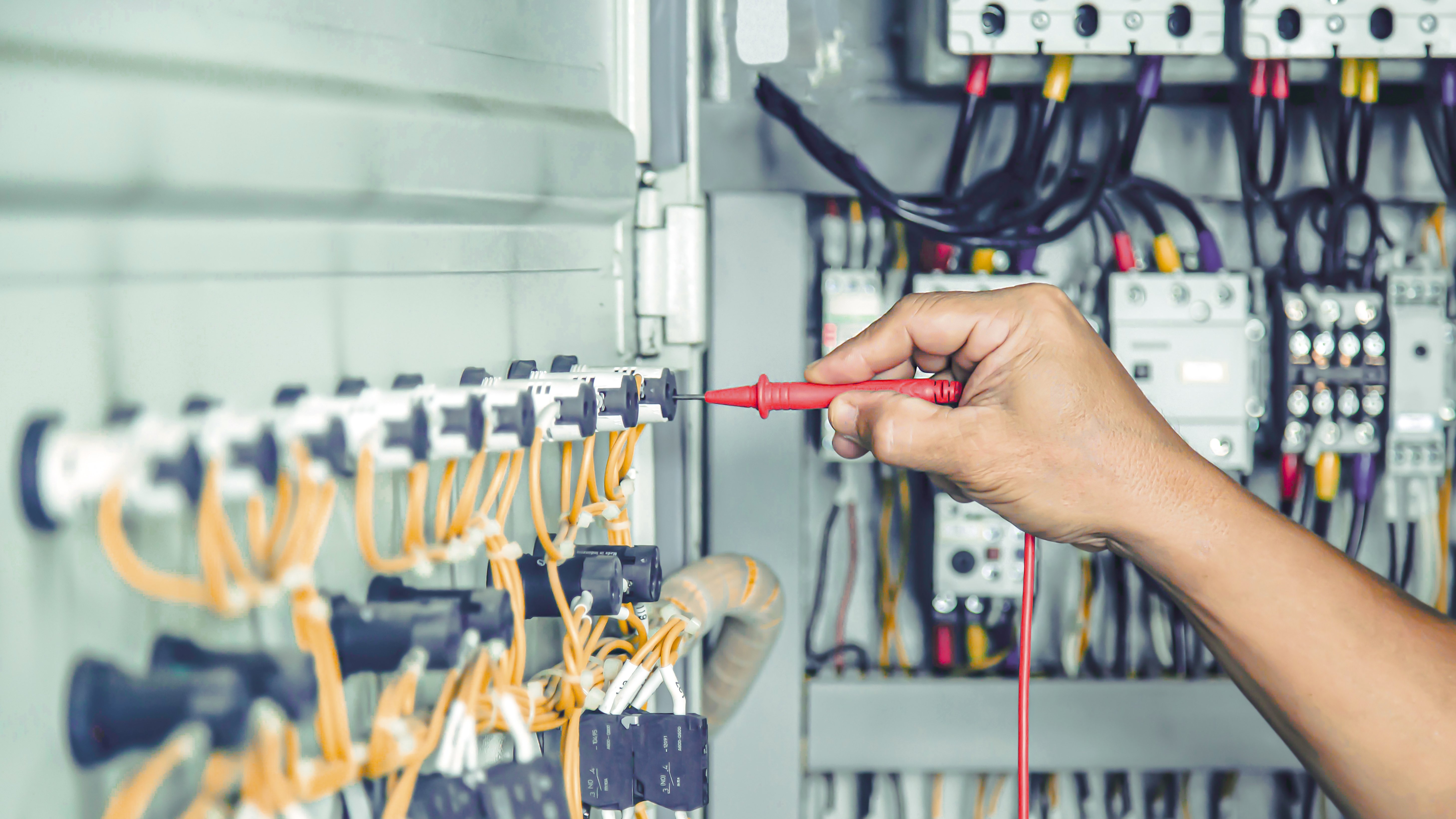 An electrical engineers hand in a wire cabinet showing the benefits of standardised electrical designs.